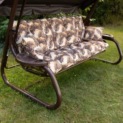 Huśtawka ogrodowa z brązowym stelażem i poduszkami w liściasty wzór. Idealna do ogrodu.