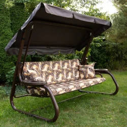 Huśtawka ogrodowa z daszkiem, przeznaczona do użytku zewnętrznego. Brązowe poduszki z roślinnym wzorem.