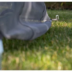 Szpilka do mocowania pokrowca na huśtawkę ogrodową, widoczna na trawie. Pokrowiec w kolorze szarym.